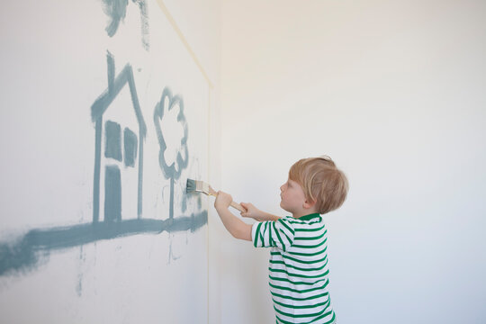 Little boy painting house and tree on wall of his new room
