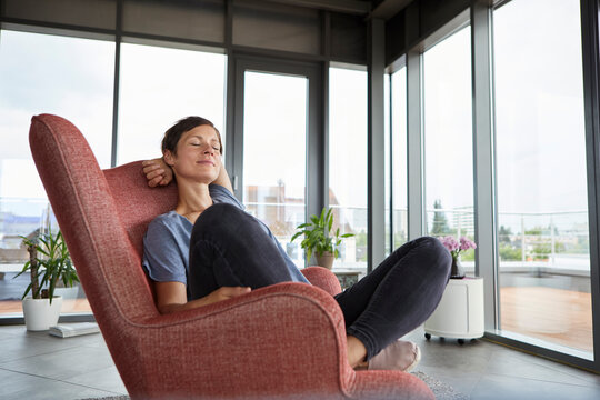 Woman sitting in armchair at home relaxing with closed eyes