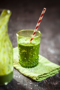 Glass of spinach smoothie with coconut milk, lemon- and orange juice and banana on napkin and wooden table