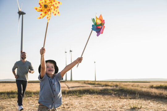 Boy with colorful pinwheels running in windpark with father following