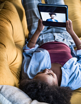 Woman relaxing on sofa at home having a video call on tablet