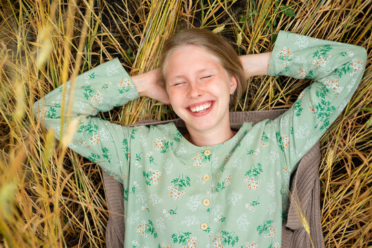Smiling woman in a vintage dress lying in a summer wheat field
