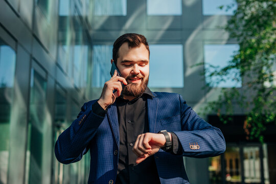Businessman talking on smartphone and checking wristwatch outdoors