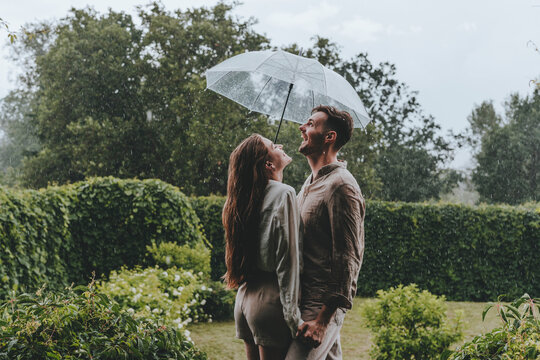Happy couple holding umbrella and enjoying in rain at garden