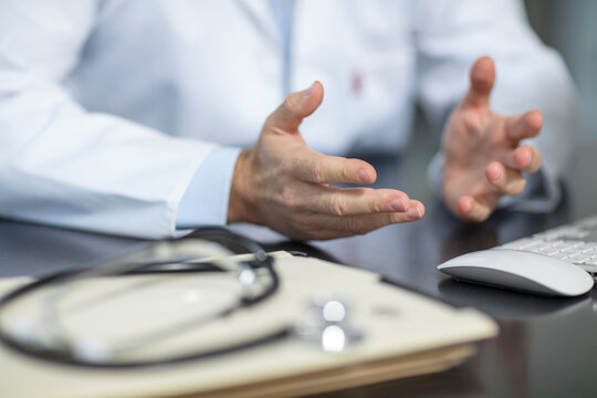Files and stethoscope on desk in medical practice with doctor gesturing