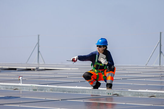 Female engineer in safety harness inspecting solar panel installation, Technician with walkie talkie during maintenance of photovoltaic system, Worker working on industrial solar power plant