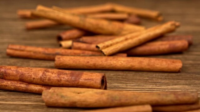 Cinnamon sticks falling and scattering across a textured wooden table surface close-up