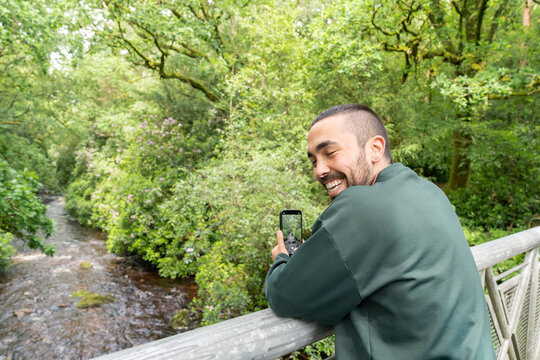 Man laughing taking smartphone picture on bridge over river