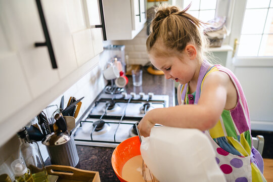Little girl pouring milk into batter, cooking pancake