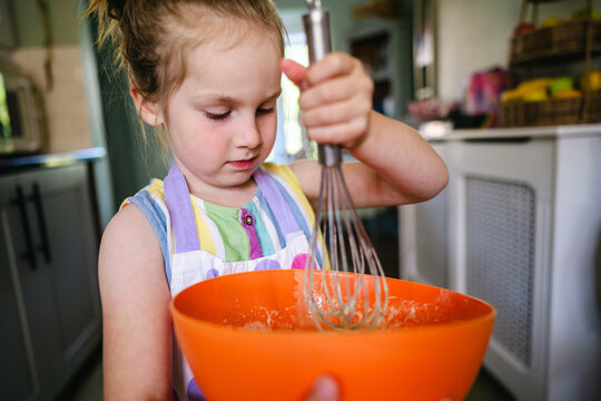 Young girl learning to cook at home, mixing batter
