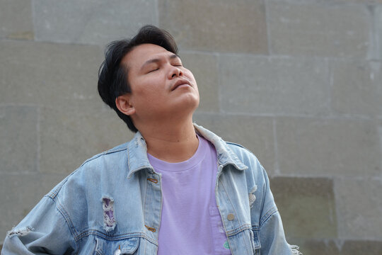 Relieved Asian Man Closing Eyes and Breathing Fresh Air Against a Stone Wall
