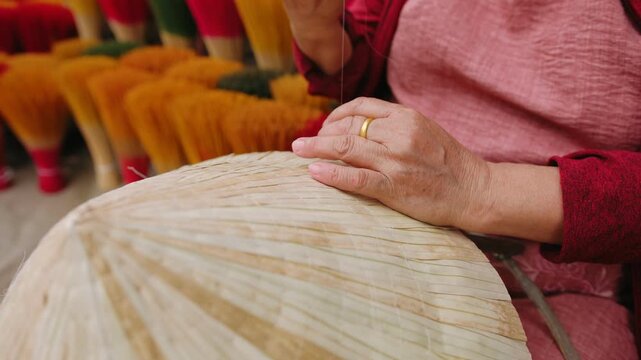 Woman making traditional conical hat with needle and thread in craft village market, Vietnam