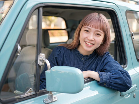 車の助手席から窓を開けて笑顔で外を眺める青い服を着た若い女性