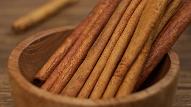 Hand placing aromatic cinnamon sticks into natural wooden bowl