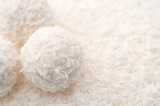 Macro close-up of homemade coconut snowball truffles on shredded coconut with soft blurred copy space. Sweet dessert, healthy vegan snack and baking ingredient concept on white background