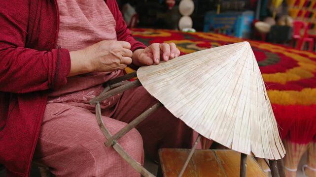 Vietnam woman making a traditional conical hat, non la, with palm leaves at an outdoor workshop in vietnam