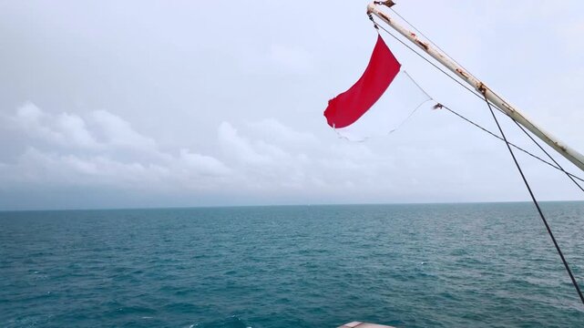 Red and white Indonesian flag waving on a boat over the open sea beneath a cloudy sky. Maritime travel scene with ocean horizon and nautical atmosphere.