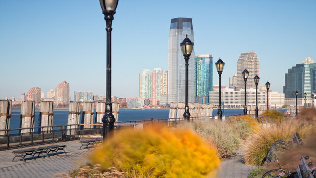 Jersey City skyline stands across the Hudson River from a quiet Manhattan waterfront promenade, representing urban exploration and travel in New York City, USA.