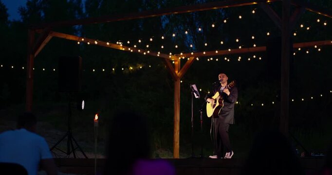 Male guitarist singing under illuminated wooden pergola at night