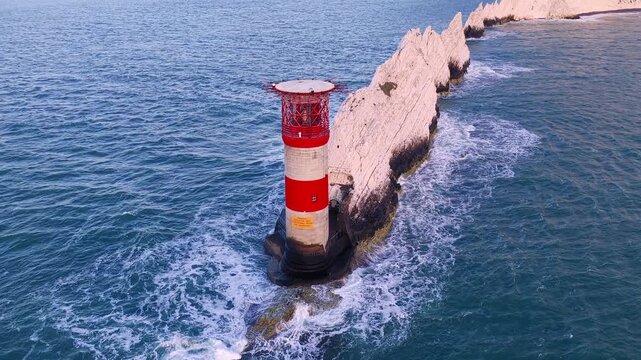 4K drone top-down panorama above The Needles Lighthouse and chalk stacks at sunset, looking toward Alum Bay on a clear summer evening off the Isle of Wight.