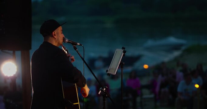 Male guitarist singing at outdoor evening concert