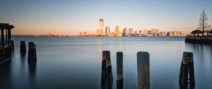 Jersey City skyline and wooden pilings on the calm Hudson River representing urban travel and tourism at sunrise in Jersey City, New Jersey, USA.