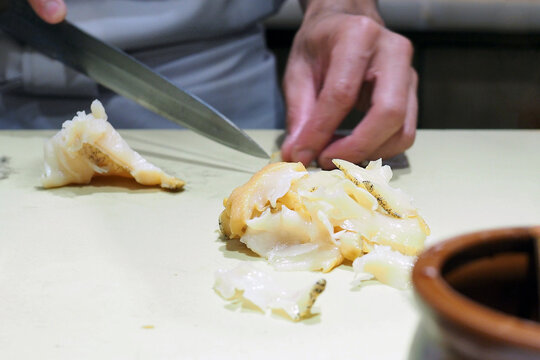 Chef slices fresh whelk Tsubugai sashimi (Sazae) with sharp knife.