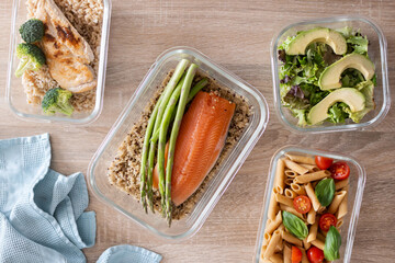 Plakat Healthy meal prep containers with salmon, chicken, pasta and fresh vegetables on kitchen table