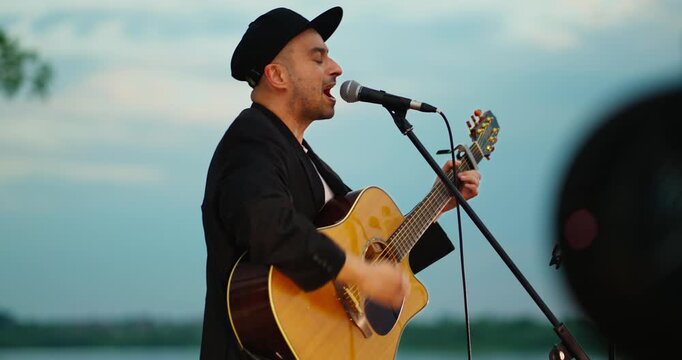Male guitarist singing on waterfront stage at dusk