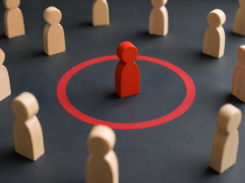 Red wooden figure standing inside a red circle separated from a crowd of neutral figures, concept for uniqueness, target audience, social isolation, individuality, and leadership.