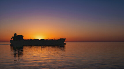 Obraz premium Oil Tanker Silhouette Sailing Across Calm Sea at Sunset Horizon