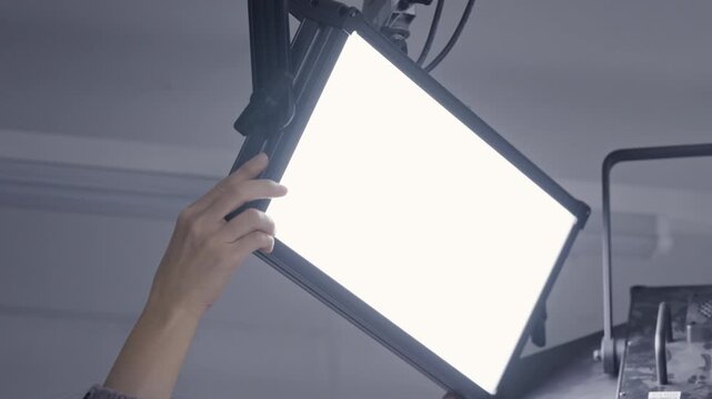 Close up of Lighting Technician Hand Adjusting Professional LED Panel Light on Studio Ceiling