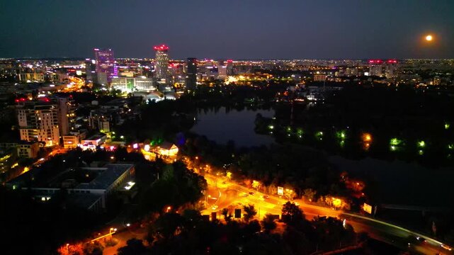 Nighttime aerial drone perspective of Bucharest cityscape, showing Herastrau park surroundings and the glowing modern office buildings in Pipera financial center, Romania.