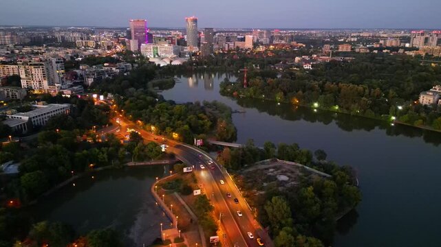 Nighttime aerial drone perspective of Bucharest cityscape, showing Herastrau park surroundings and the glowing modern office buildings in Pipera financial center, Romania.