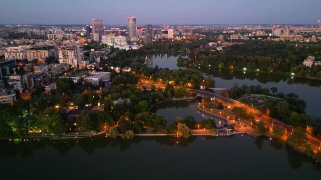 Nighttime aerial drone perspective of Bucharest cityscape, showing Herastrau park surroundings and the glowing modern office buildings in Pipera financial center, Romania.