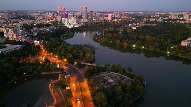 Nighttime aerial drone perspective of Bucharest cityscape, showing Herastrau park surroundings and the glowing modern office buildings in Pipera financial center, Romania.