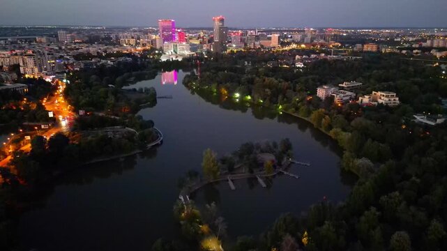 Nighttime aerial drone perspective of Bucharest cityscape, showing Herastrau park surroundings and the glowing modern office buildings in Pipera financial center, Romania.