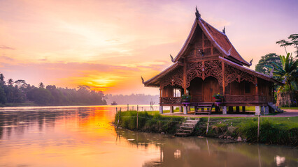 Obraz premium A traditional Limas house stands on a tranquil riverbank at sunset, reflecting the luminous sky, intricate wooden architecture, and an elegant cultural heritage scene.