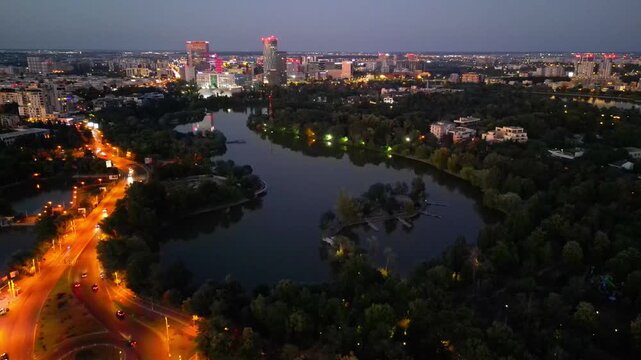 Nighttime aerial drone perspective of Bucharest cityscape, showing Herastrau park surroundings and the glowing modern office buildings in Pipera financial center, Romania.