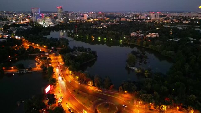 Nighttime aerial drone perspective of Bucharest cityscape, showing Herastrau park surroundings and the glowing modern office buildings in Pipera financial center, Romania.