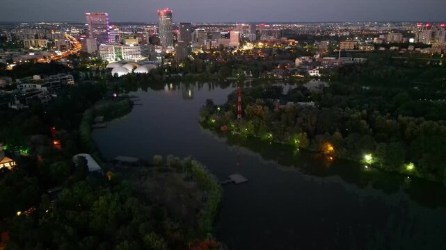 Nighttime aerial drone perspective of Bucharest cityscape, showing Herastrau park surroundings and the glowing modern office buildings in Pipera financial center, Romania.