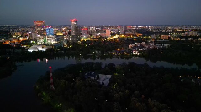 Nighttime aerial drone perspective of Bucharest cityscape, showing Herastrau park surroundings and the glowing modern office buildings in Pipera financial center, Romania.