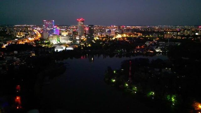 Nighttime aerial drone perspective of Bucharest cityscape, showing Herastrau park surroundings and the glowing modern office buildings in Pipera financial center, Romania.