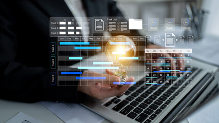 Fototapeta premium Business professional showcases a light bulb symbolizing innovation against a digital project management dashboard on a laptop, highlighting productivity and organization. Gantry