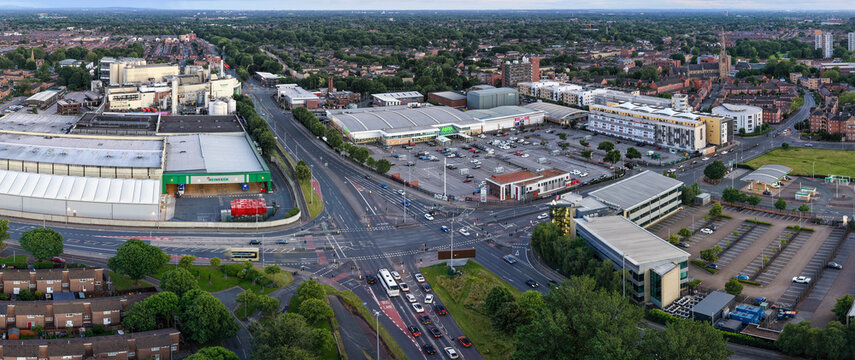 Aerial panorama over Manchester, highlighting Princess Road traffic, Hulme Retail Park with the Asda Superstore, and the Heineken brewery complex at dusk.