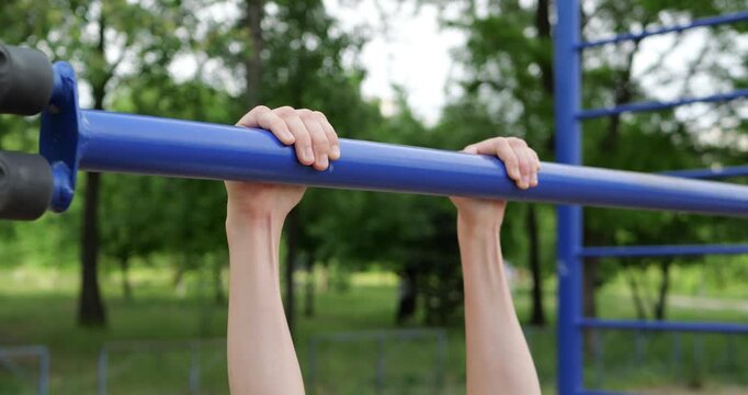 Fitness enthusiast performs pull-ups on outdoor gym equipment. Strong hands grip bar firmly. Healthy lifestyle and workout motivation captured in bright park setting.