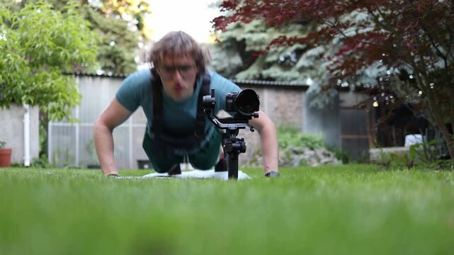 Young videographer performs push ups beside a gimbal stabilizer on grass building upper body strength endurance and stamina for long filming 