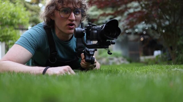 Determined paparazzi crawls low across the grass with camera stabilizer tracking a hidden subject Seeking exclusive content and attention grabbing media coverage