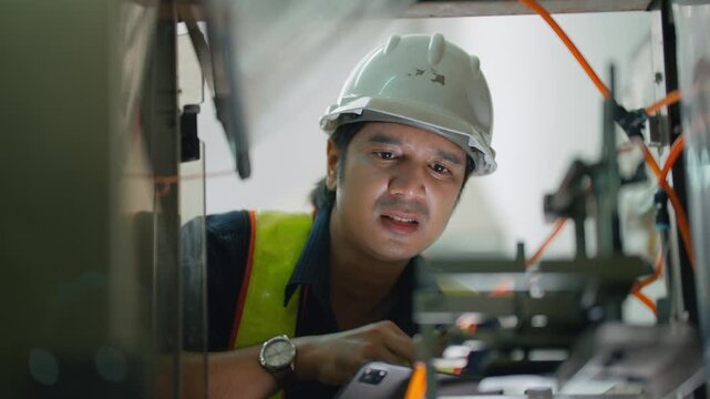Focused Technician at Work: A diligent technician wearing a hard hat and safety vest inspects complex machinery, his brow furrowed in concentration as he performs his critical task.