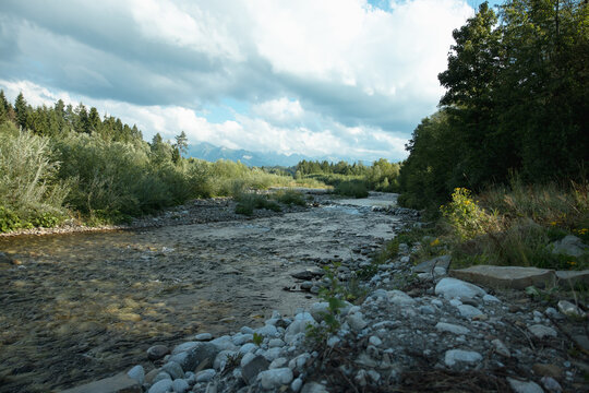 Mountain river flowing through forest valley with dramatic clouds and distant peaks